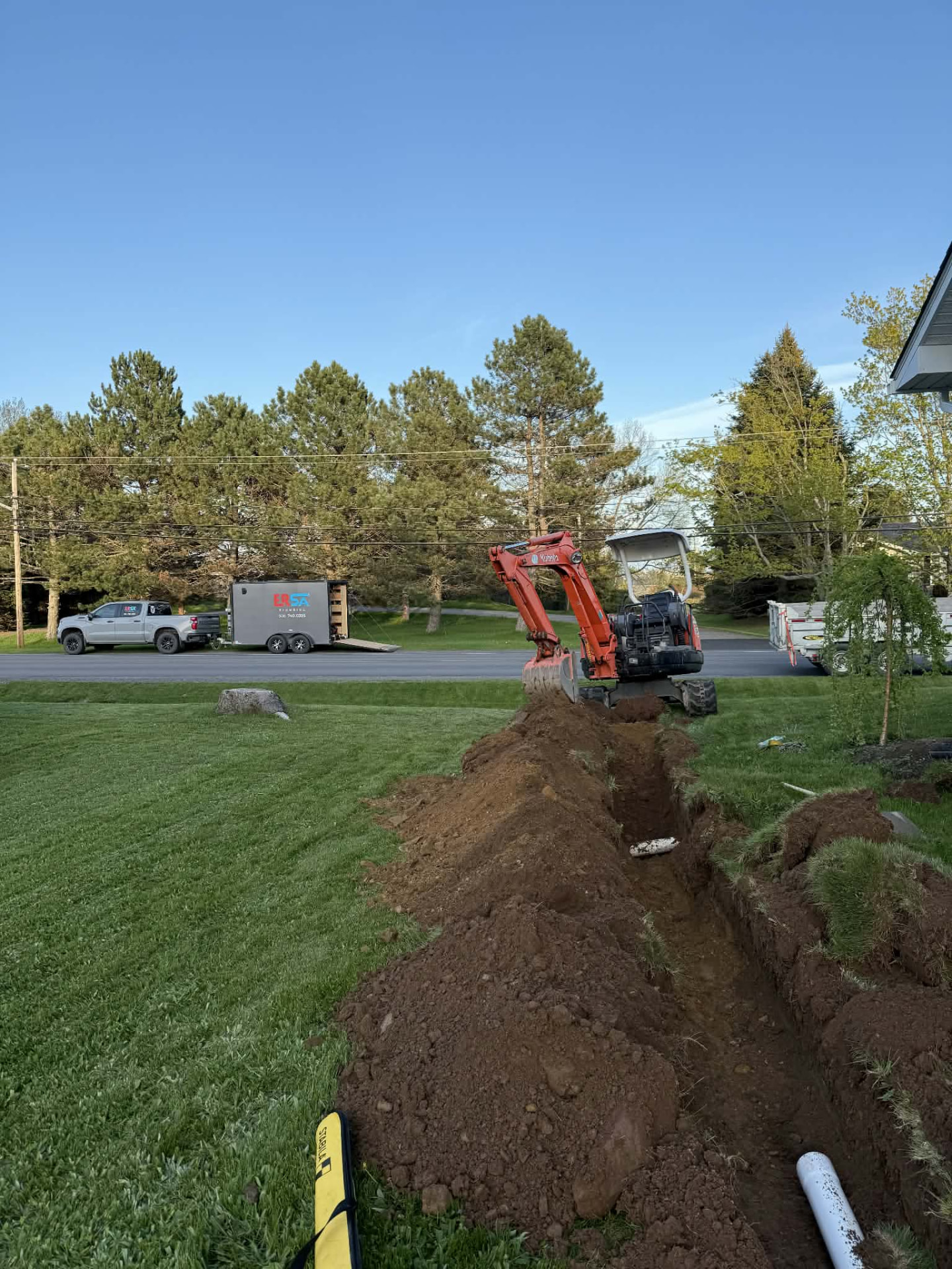 Orange Kubota mini-excavator digging a trench for PVC water pipe during a residential plumbing repair