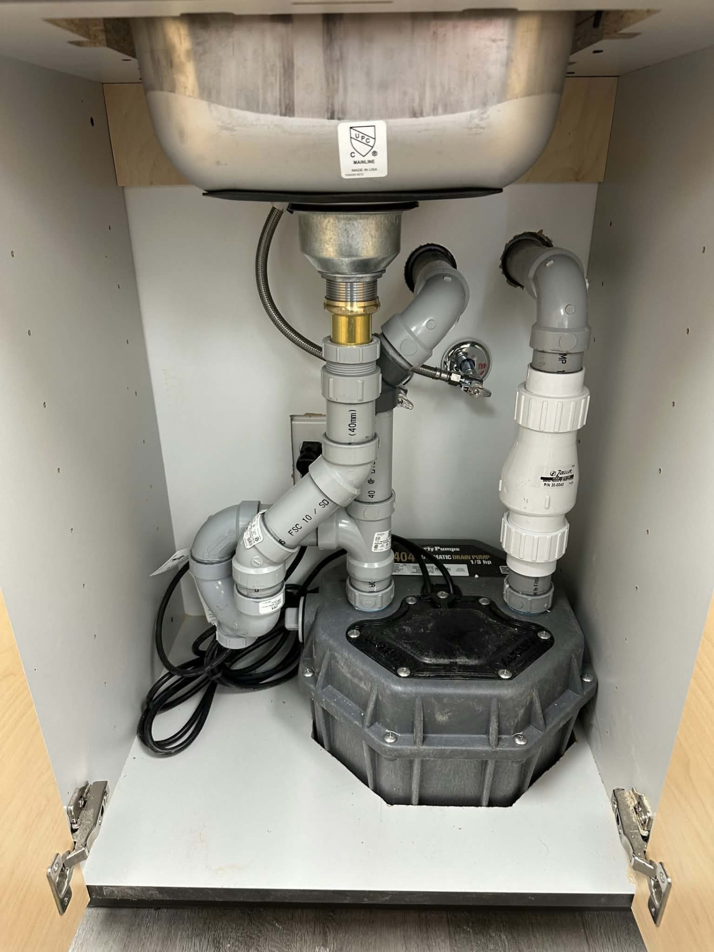 Automatic drain pump and PVC piping installed under a sink by ERSA Plumbing