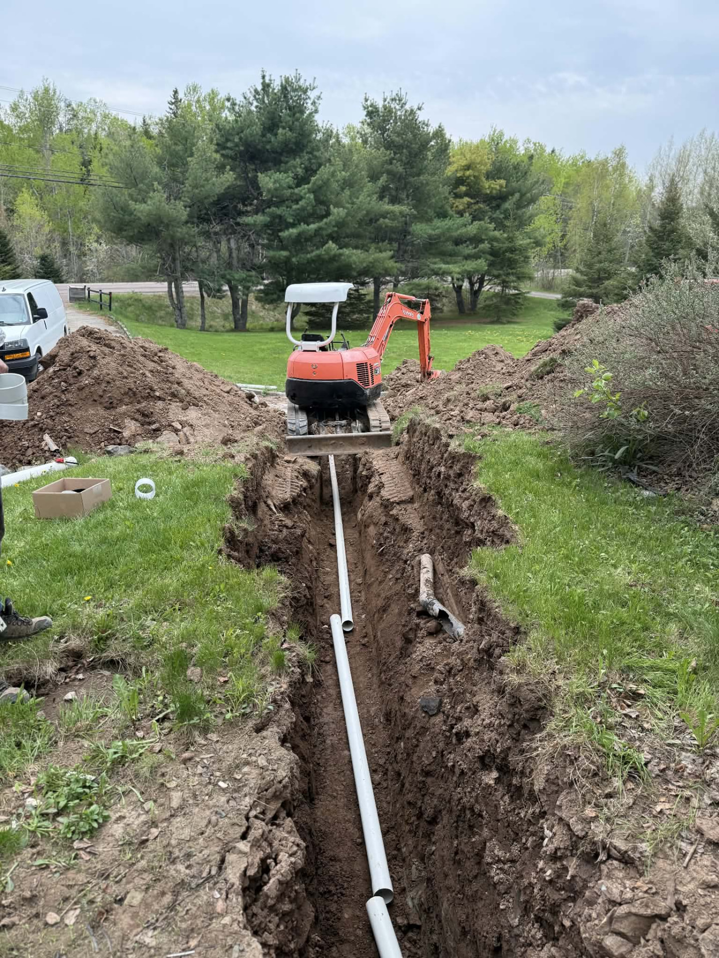 Trench running down a lawn with white PVC pipe and a white service van in the background during a plumbing repair