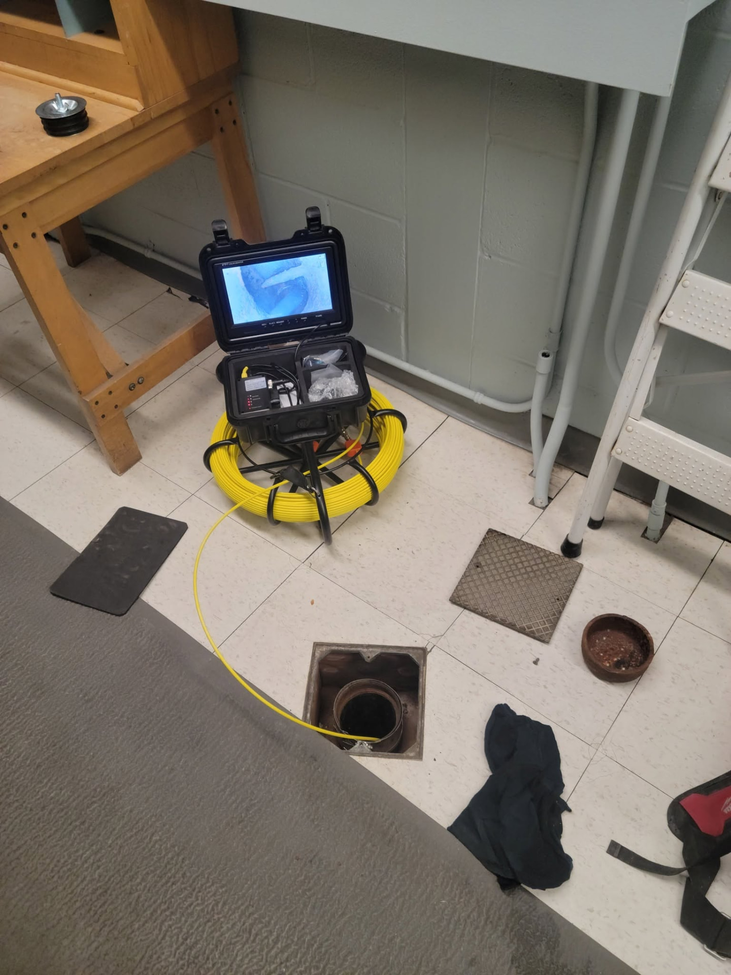 Sewer camera inspection system with a yellow cable fed into an open floor drain to inspect subsurface piping