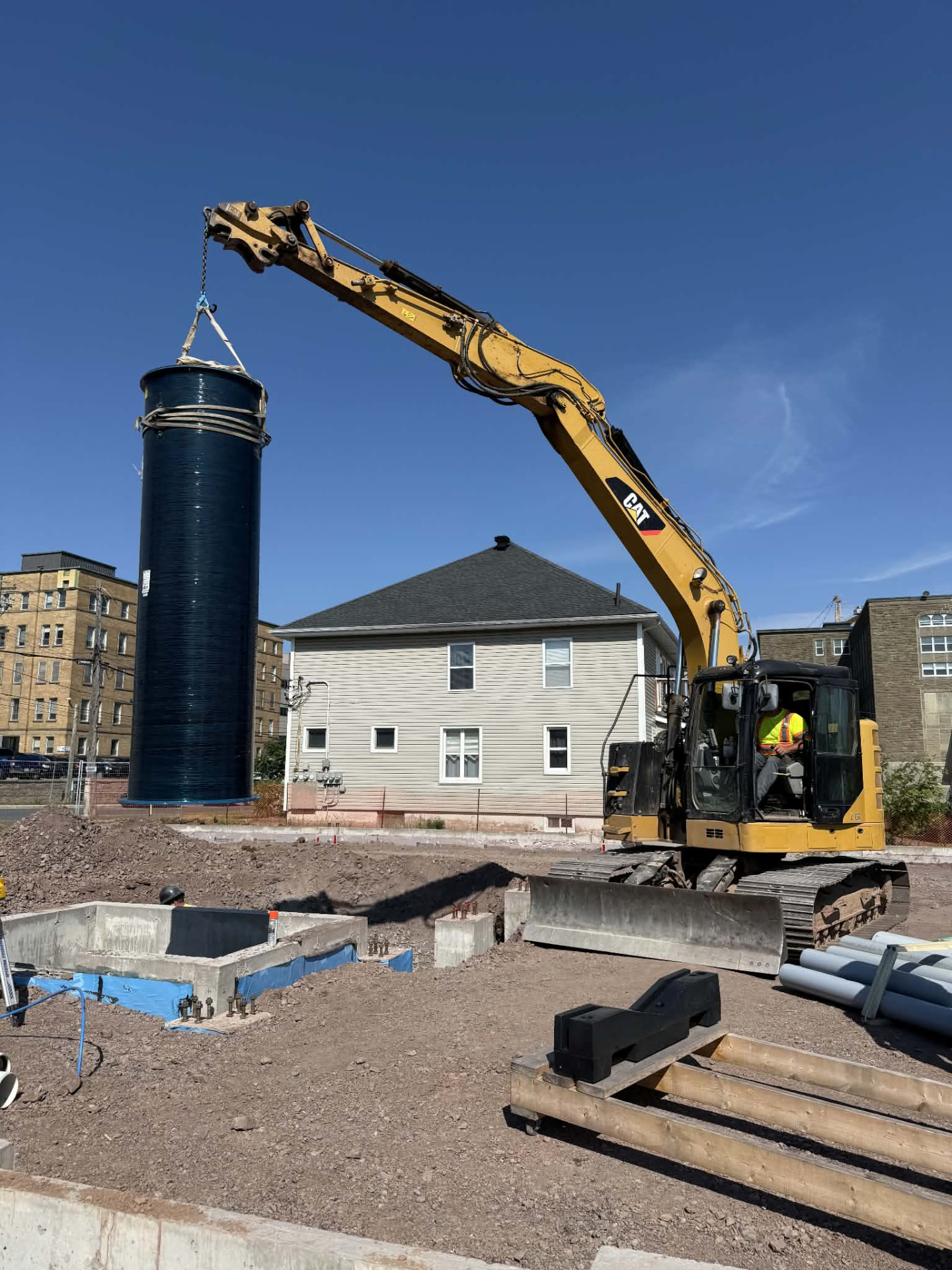 Excavator lowering a large water and sewer service shaft into place on a commercial construction site
