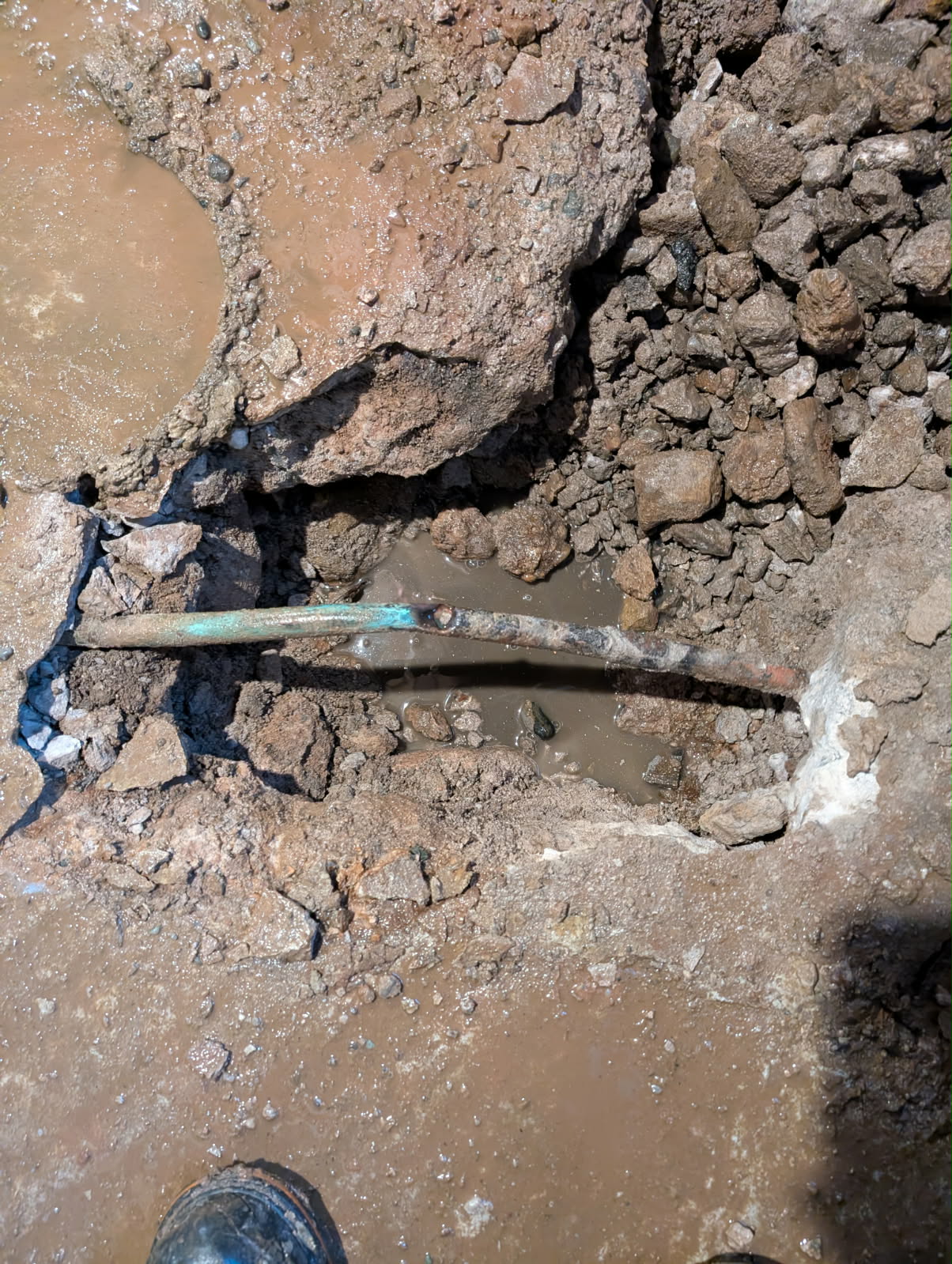 Corroded copper pipe with a leak repaired in an excavated trench during an emergency call