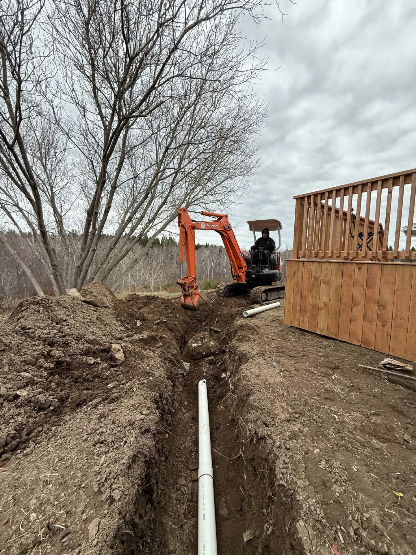Trench with white PVC pipe laid beside a wooden structure during a residential water pipe repair