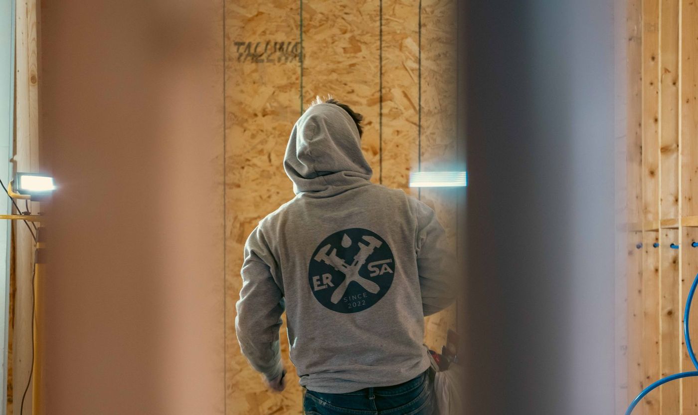 Plumber completing a plumbing rough-in inside a framed building